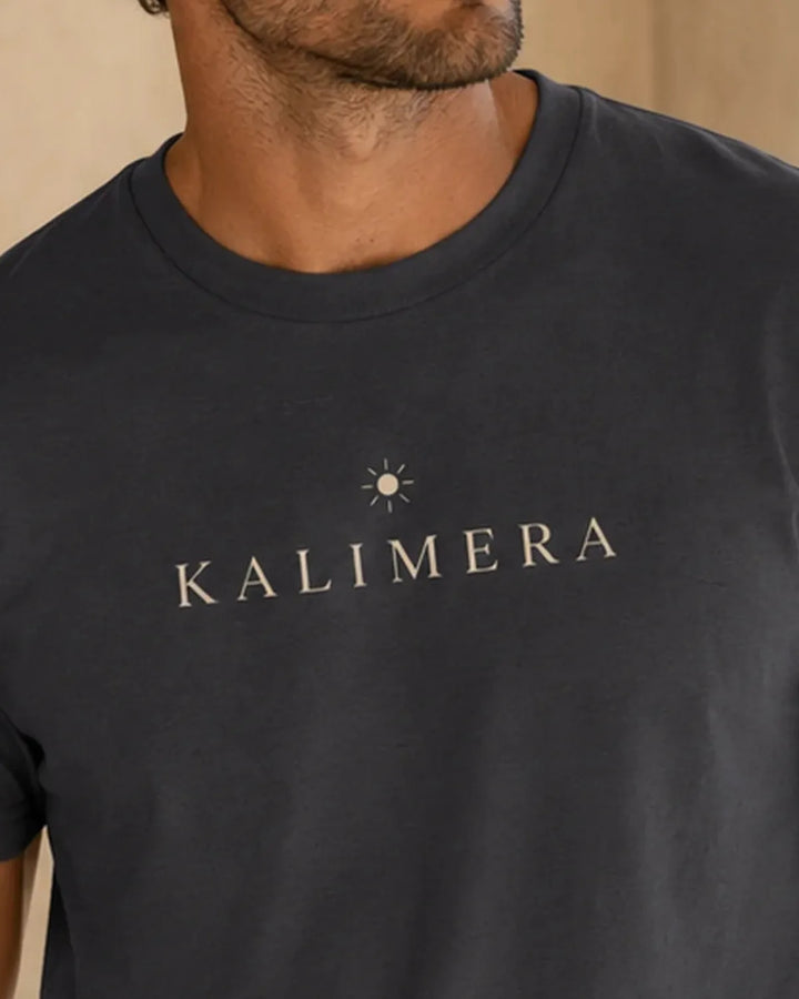 Model wearing navy KALIMERA T-shirt in a relaxed Mediterranean summer setting