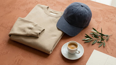 Italian-inspired apparel flat lay with folded sweatshirt, cotton cap and espresso on warm terracotta surface