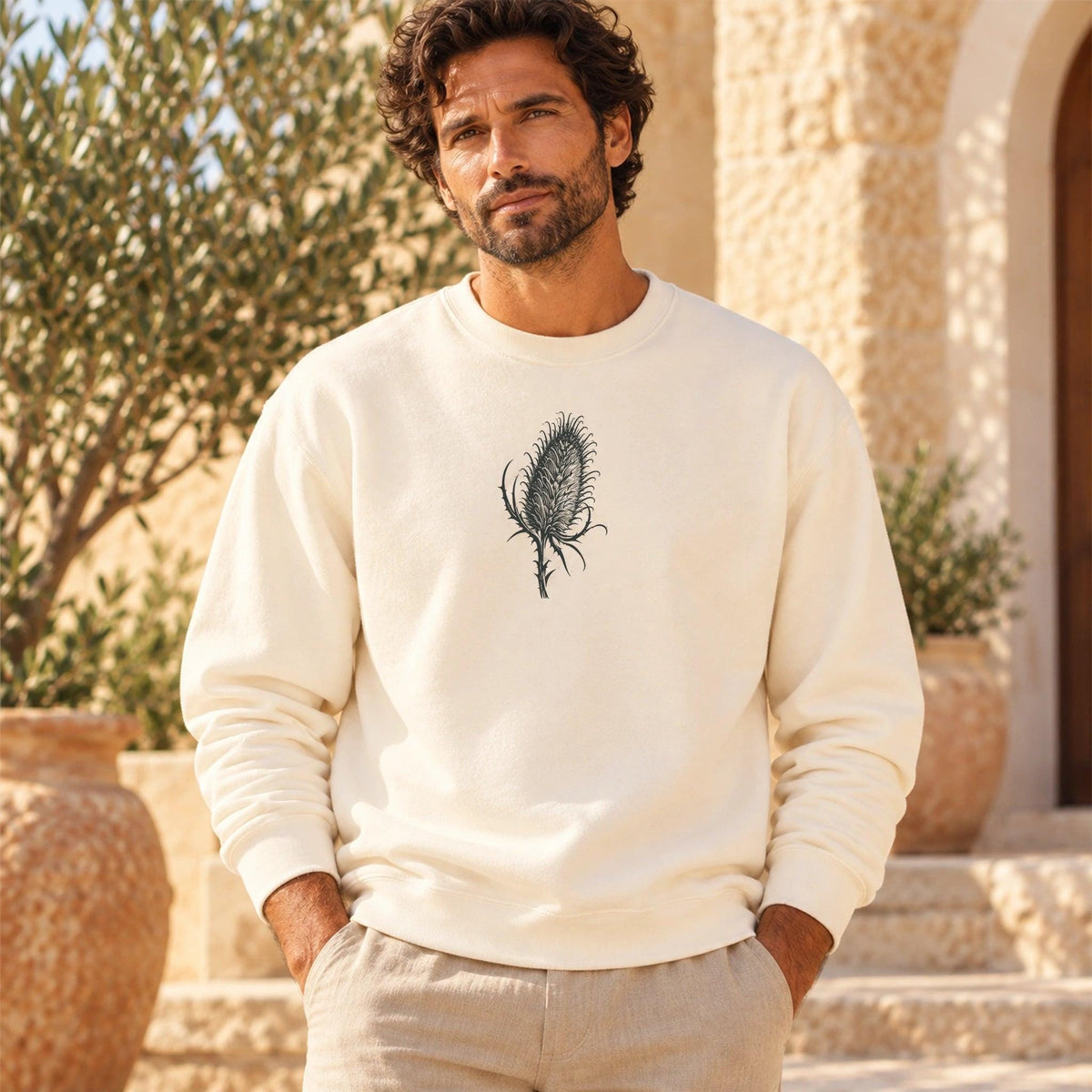 Male model wearing Cardó Ivory crewneck with original centered charcoal botanical print, Mediterranean courtyard