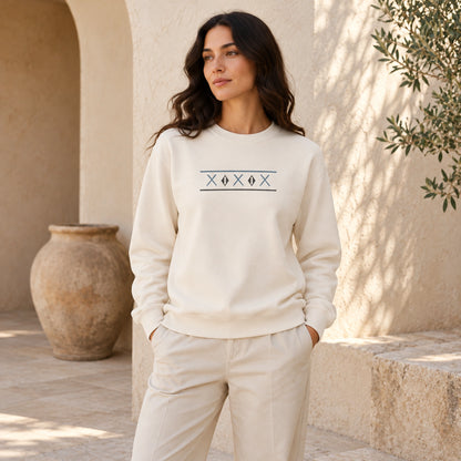 Female model wearing the Tinos Dovecote Geometry Ivory crewneck in a Mediterranean courtyard