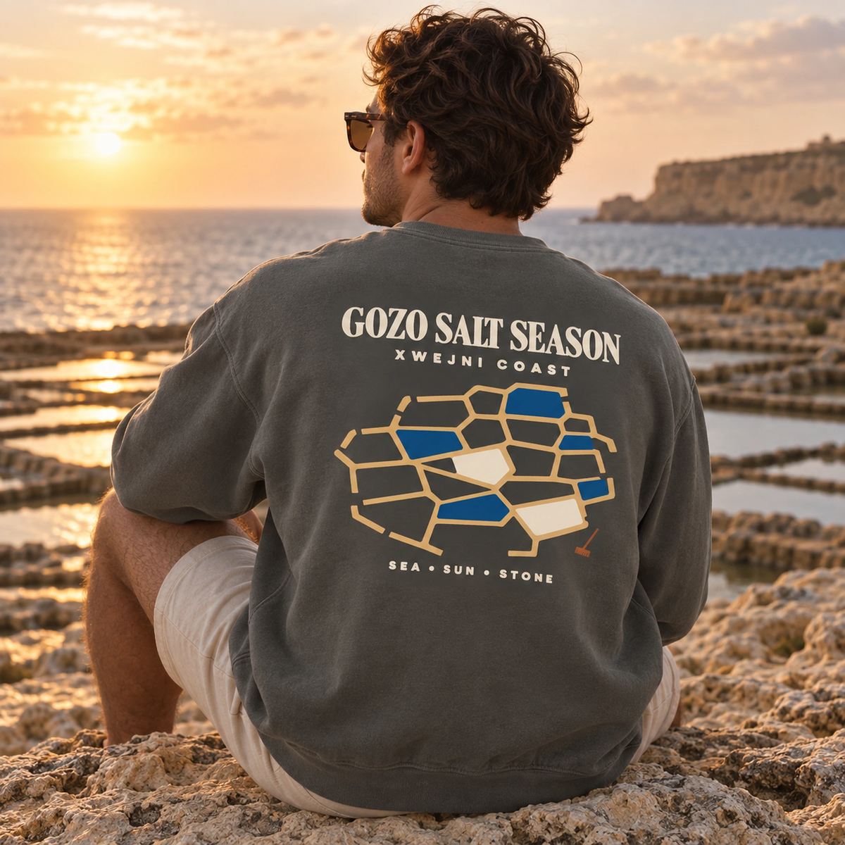 Lifestyle view of the Gozo Salt Season Comfort Colors 1566 sweatshirt in Pepper with the Xwejni Coast design shown accurately.