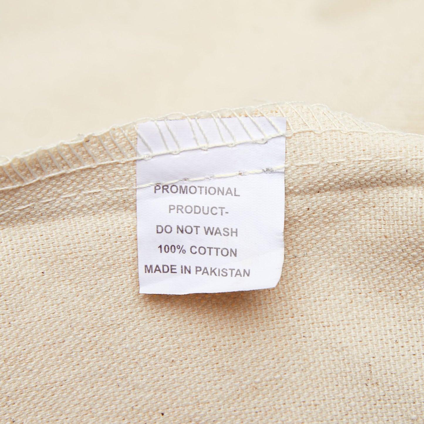 Label on a beige fabric product indicating 'Promotional Product, Do Not Wash, 100% Cotton, Made in Pakistan'.