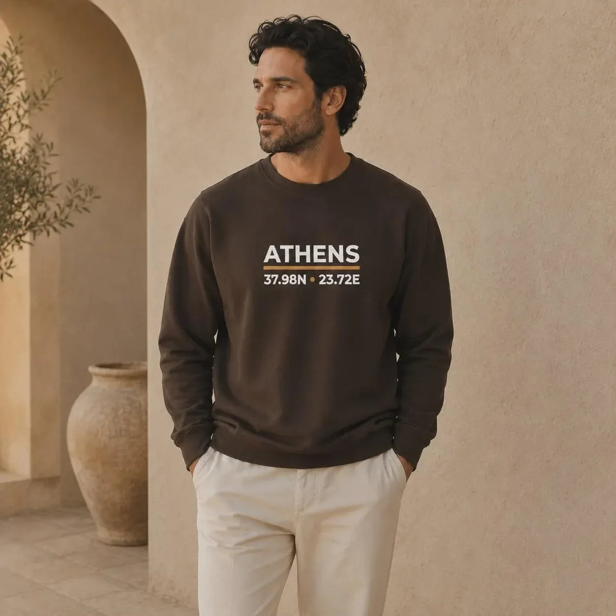 A man wearing a dark brown crewneck sweatshirt with 'ATHENS 37.98N .