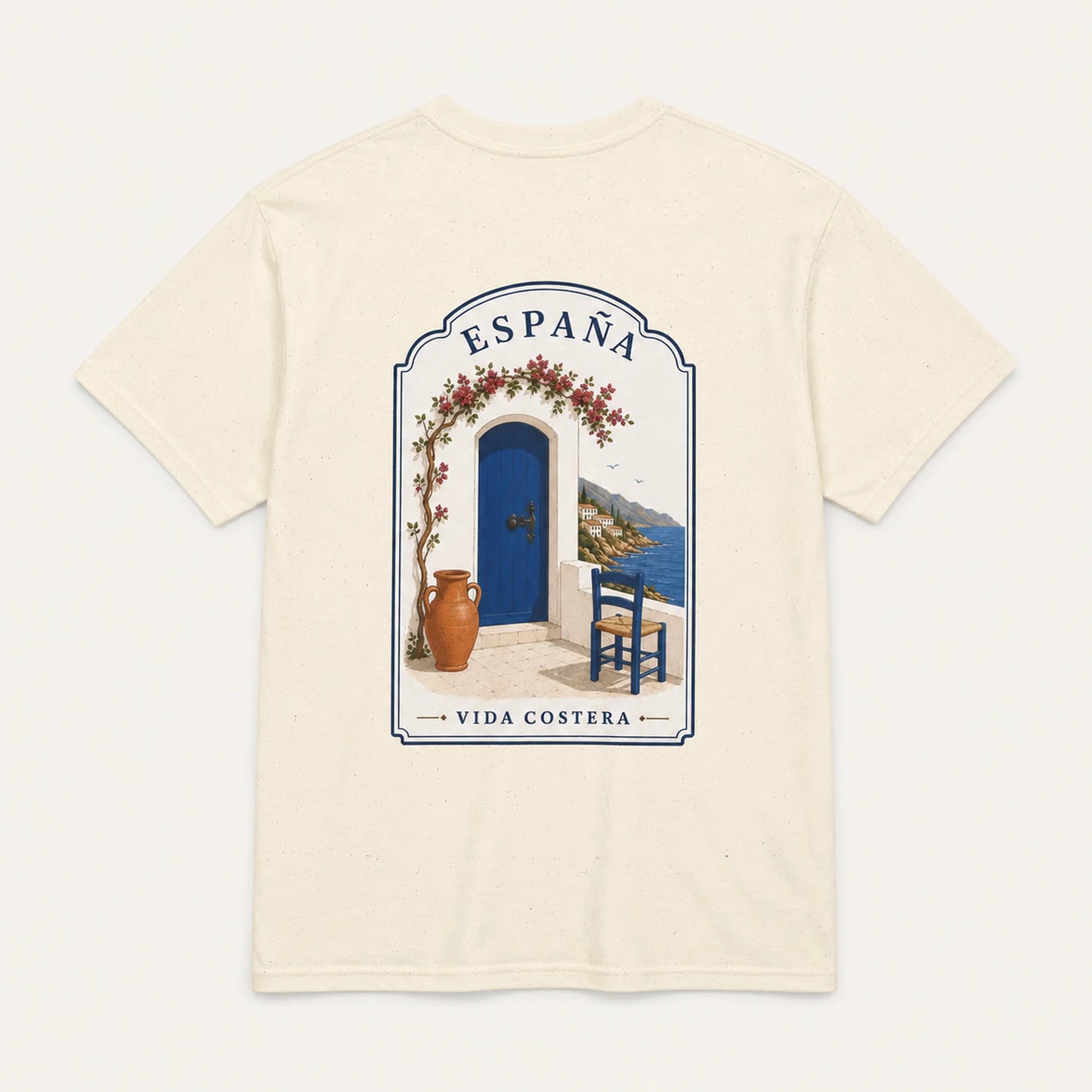 An off-white short-sleeve t-shirt with a large graphic print on the back depicting a Mediterranean scene with a blue door, blue sky, and the text 'ESPAÑA' and 'VIDA COSTERA'.