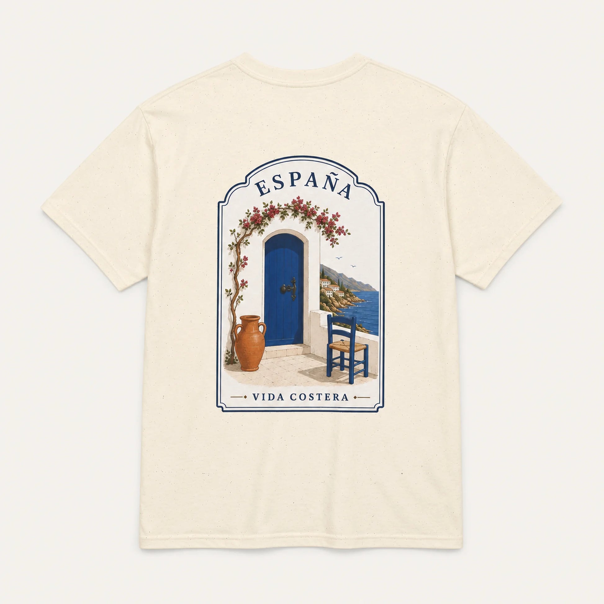 An off-white short-sleeve t-shirt with a large graphic print on the back depicting a Mediterranean scene with a blue door, blue sky, and the text 'ESPAÑA' and 'VIDA COSTERA'.