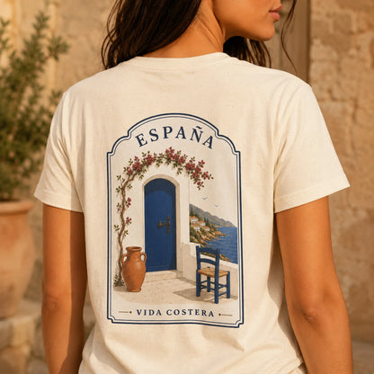 TP HERO: A woman shown from behind wearing a cream-colored t-shirt with a graphic print of a blue door, blue chair, and terracotta vase under the text 'ESPAÑA VIDA COSTERA'.