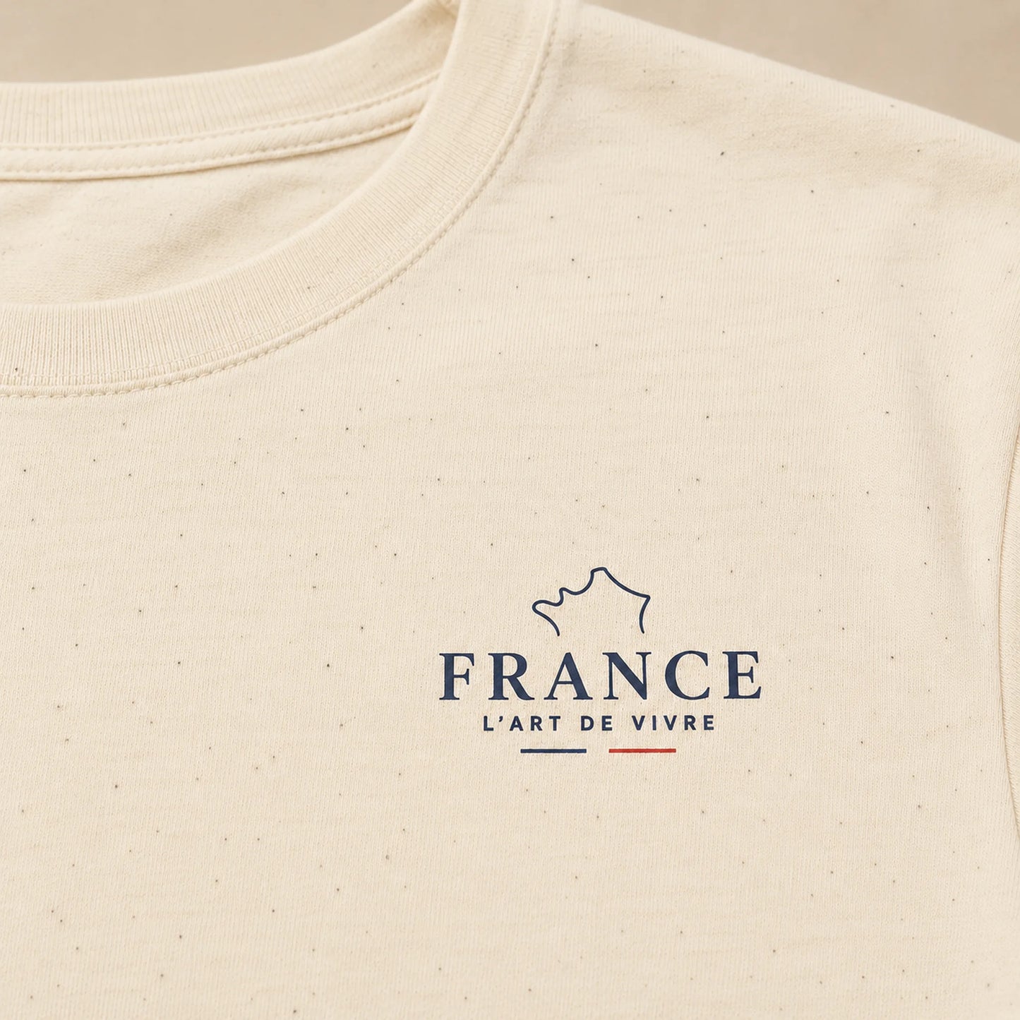 Close-up of a cream-colored textured t-shirt featuring a navy blue graphic of the map of France with the text 'FRANCE L'ART DE VIVRE' and a small red accent line.
