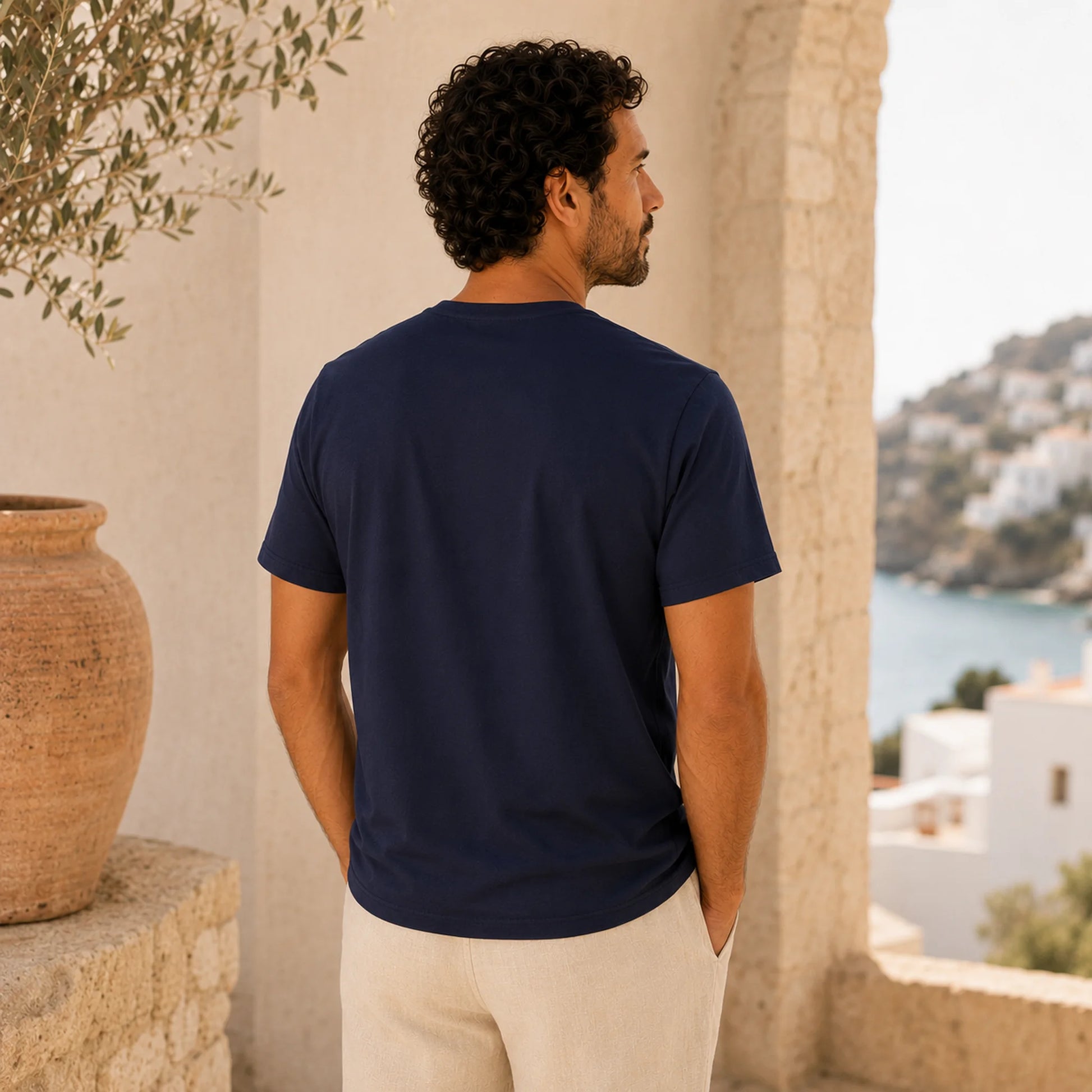 Man wearing a navy blue t-shirt standing in a scenic location with a view of the sea and buildings.