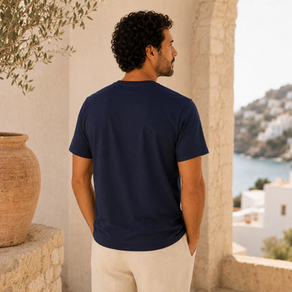 Man wearing a navy blue t-shirt standing in a scenic location with a view of the sea and buildings.