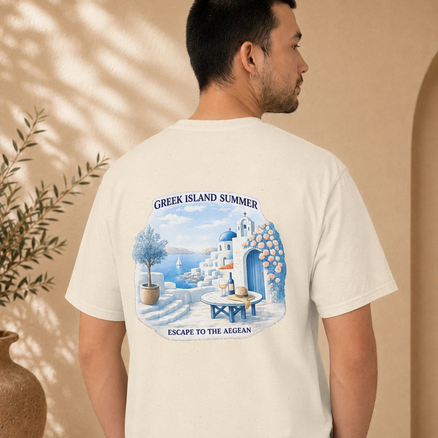 TP HERO: A man wearing a cream-colored t-shirt, viewed from the back. The shirt features a large graphic print of a Greek island summer scene with white buildings, blue domes, and a blue table with a bottle, framed by the text 'GREEK ISLAND SUMMER' and 'ESCAPE TO THE AIGEAN'.
