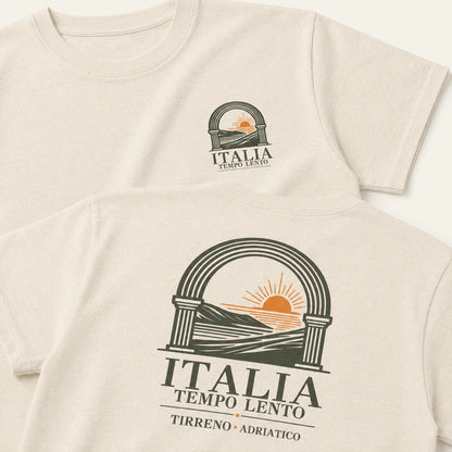 Two cream-colored short-sleeve t-shirts shown in a flat-lay arrangement, displaying the front and back of the design. The design features a dark green arch graphic with a yellow-orange rising sun over hills, with the text 'ITALIA TEMPO LENTO' and 'TIRRENO • ADRIATICO'.