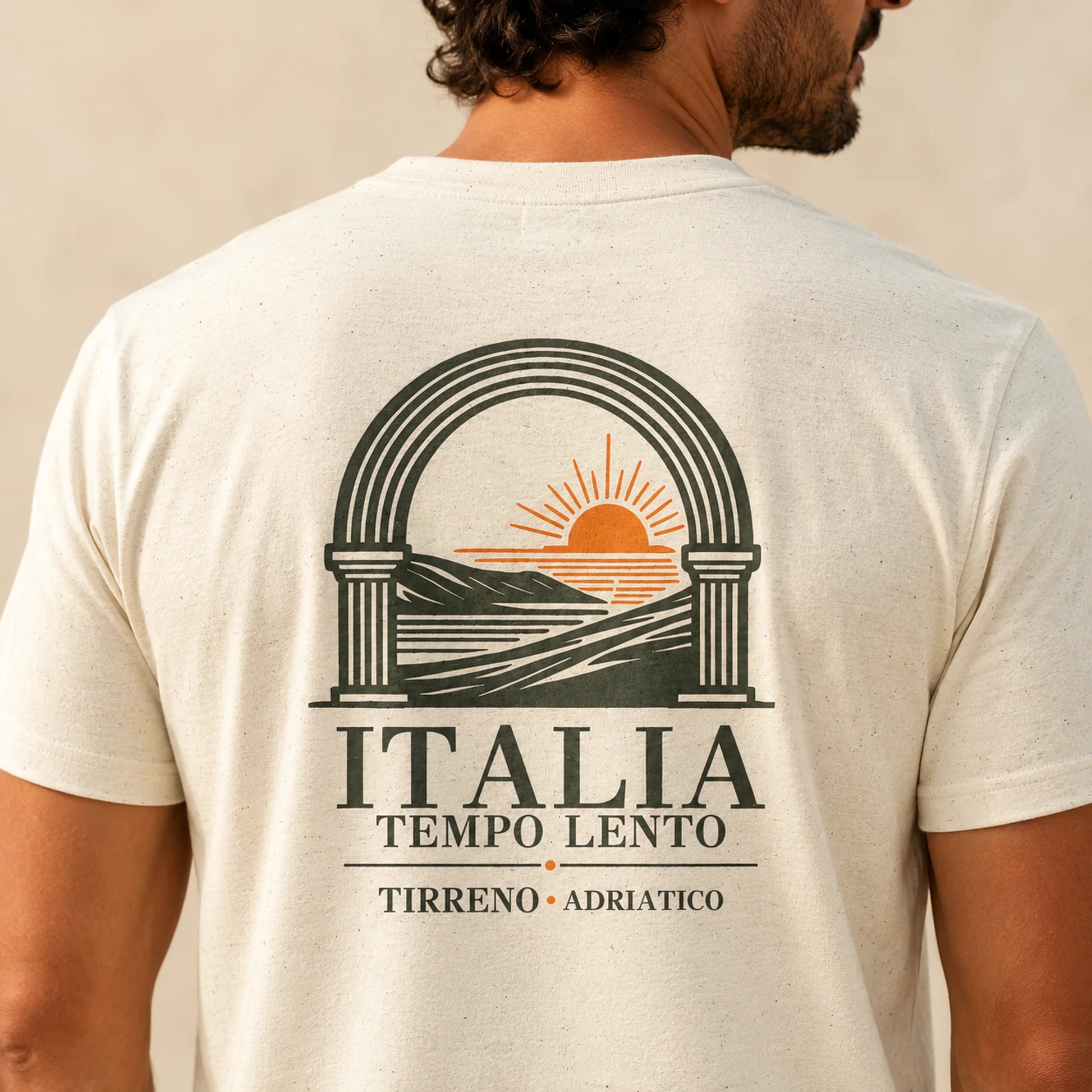 TP HERO: A man wearing a cream-colored t-shirt, viewed from the back. The shirt features a large graphic print of an Italian coastal landscape with an arch, sun, and waves, accompanied by the text 'ITALIA TEMPO LENTO' and 'TIRRENO • ADRIATICO'.