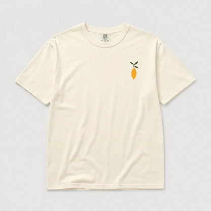 An off-white short-sleeve crewneck t-shirt featuring a small embroidered lemon graphic with green leaves on the left chest, displayed flat against a light gray background.