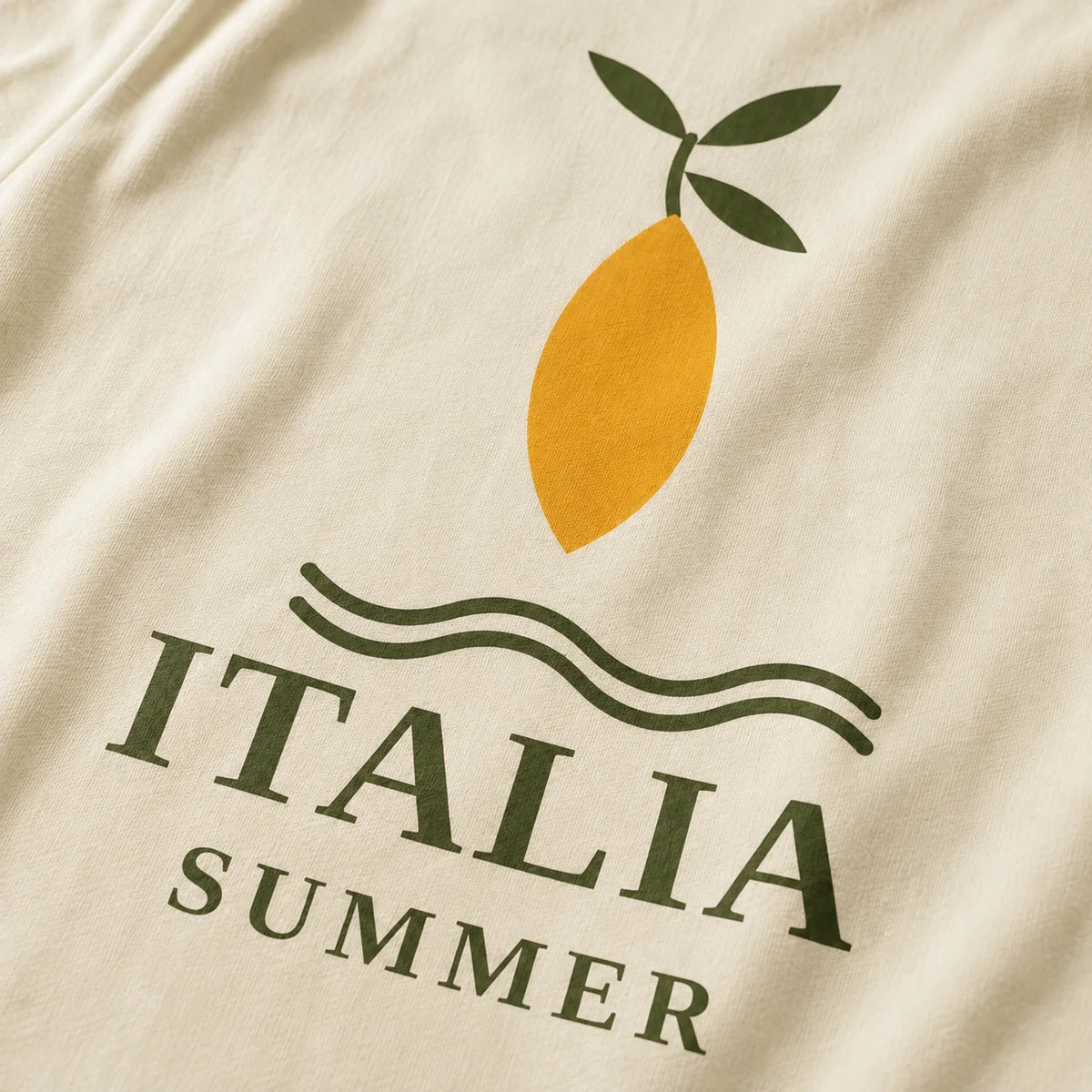 Close-up of a cream-colored fabric surface featuring a printed graphic of a yellow lemon with green leaves above the words 'ITALIA SUMMER' in dark green.