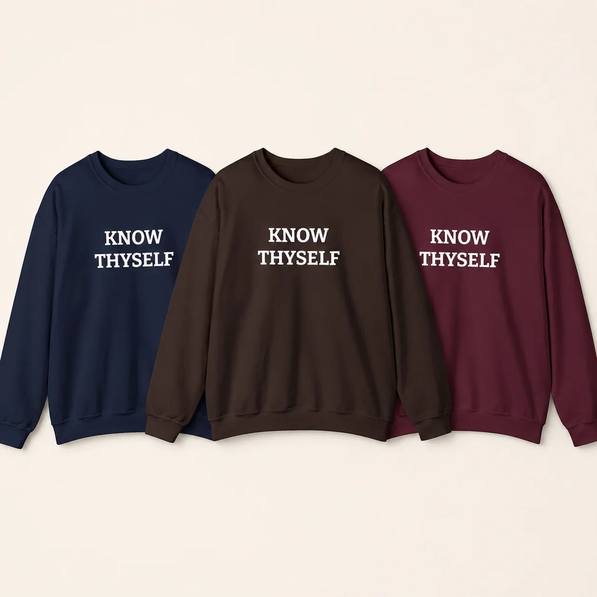 Three crewneck sweatshirts in navy blue, dark brown, and burgundy, each embroidered with the white text 'KNOW THYSELF' on the chest, displayed against a light beige background.