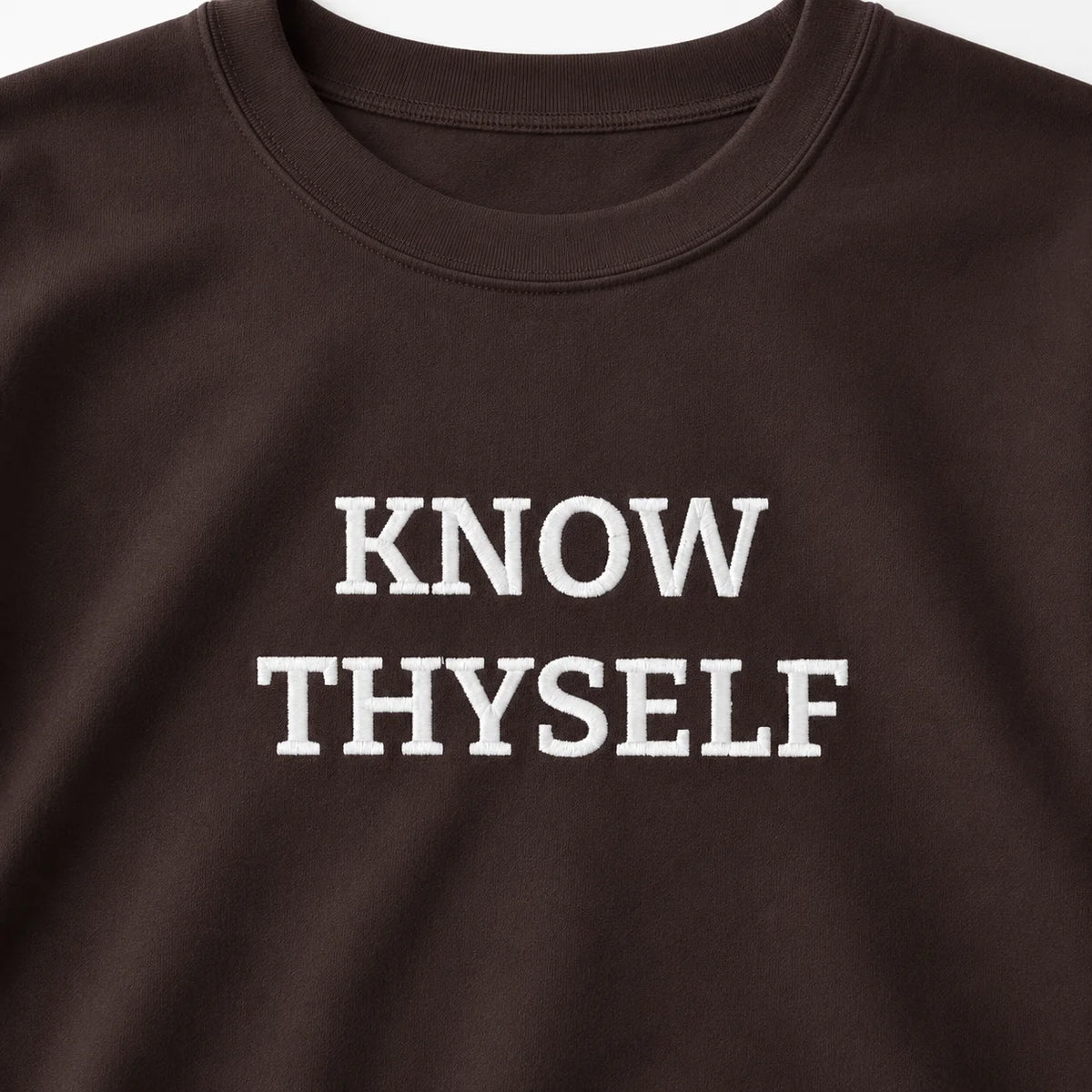 Close-up of the Dark Chocolate Know Thyself crewneck sweatshirt with the white embroidered KNOW THYSELF chest design.