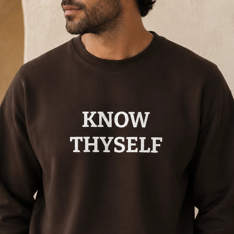 TP HERO: A close-up of a man wearing a dark brown crewneck sweatshirt with the text 'KNOW THYSELF' embroidered in white block letters across the chest.