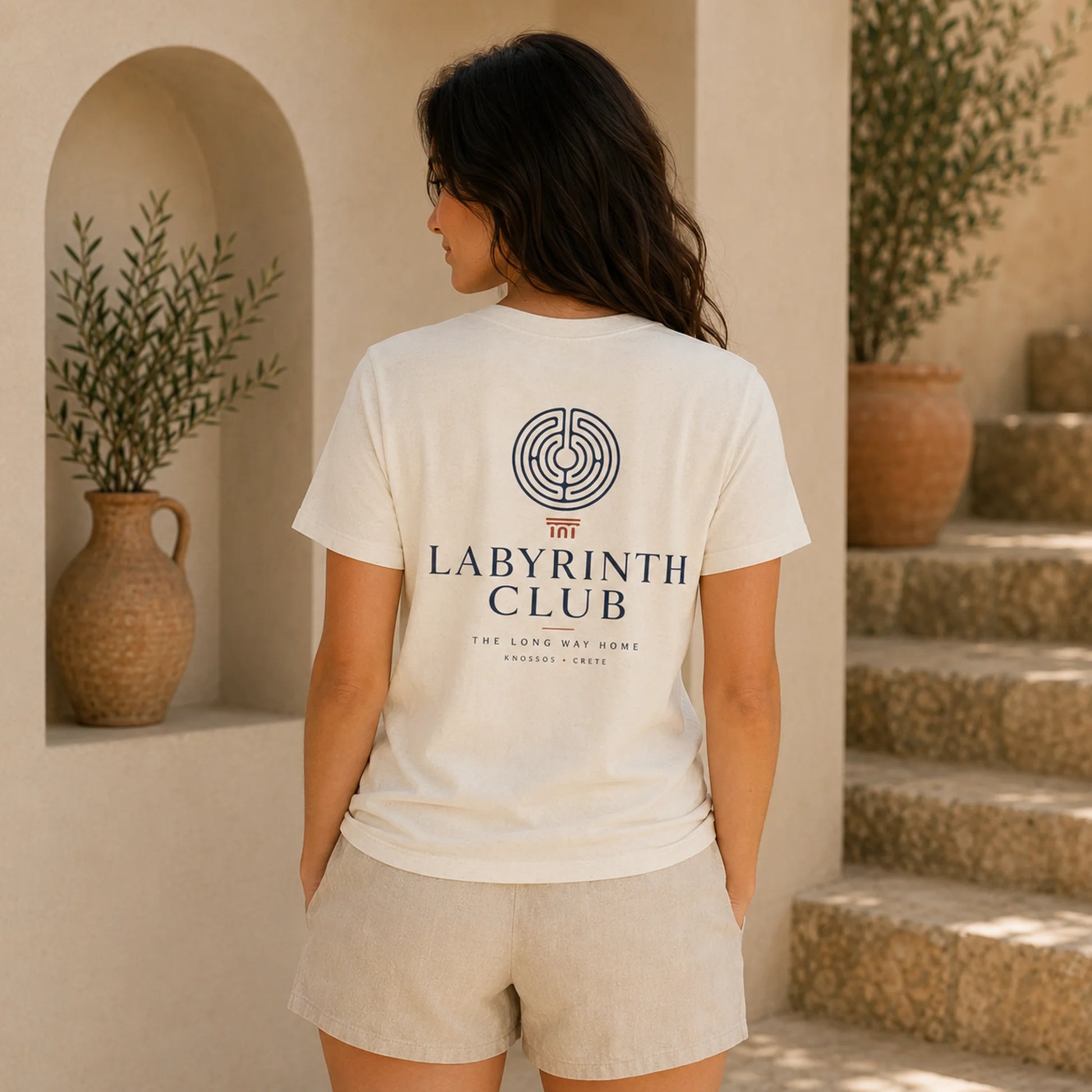 Woman wearing a 'Labyrinth Club' t-shirt in a warm, indoor setting with plants and steps.
