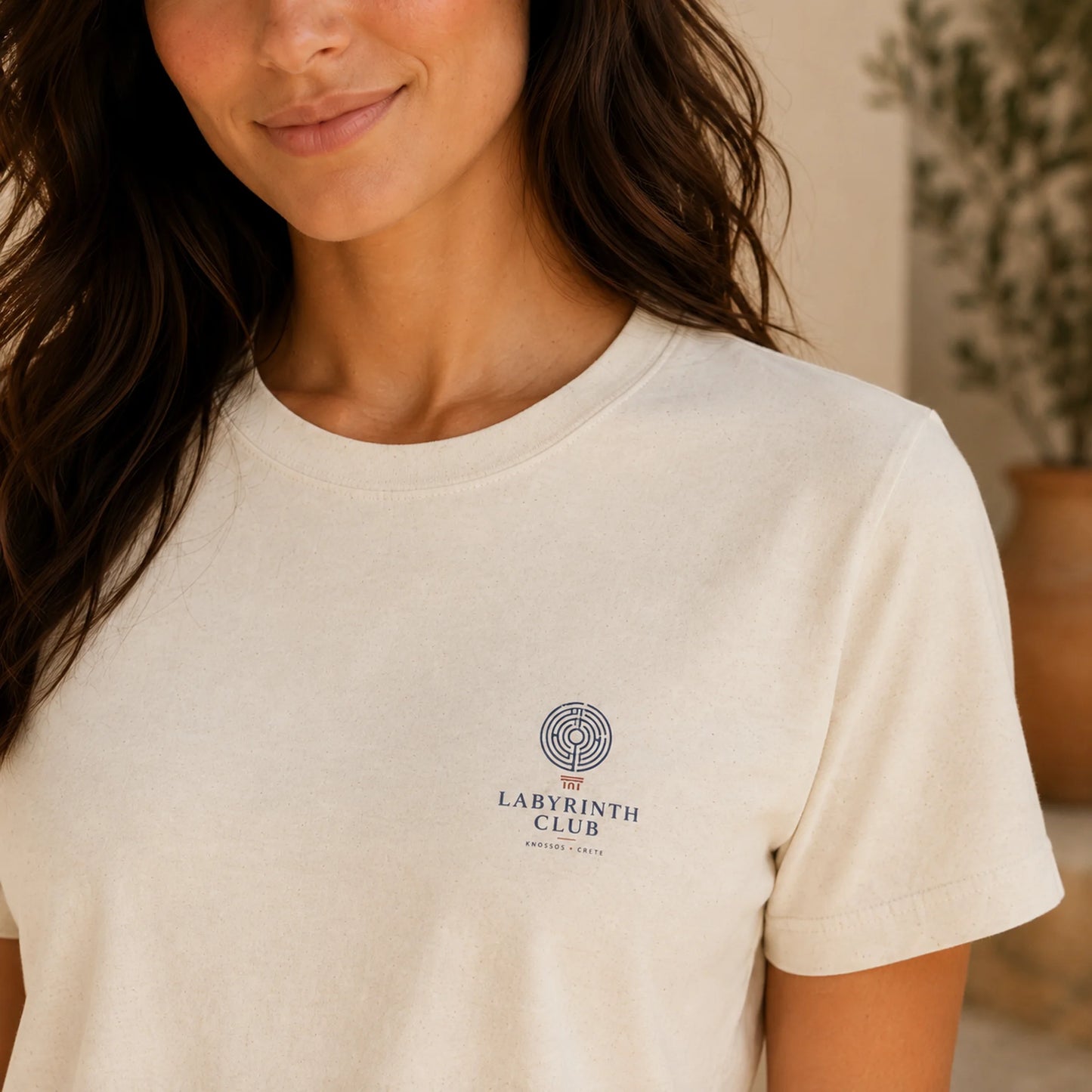 Woman wearing a beige t-shirt with a logo on it, standing indoors.