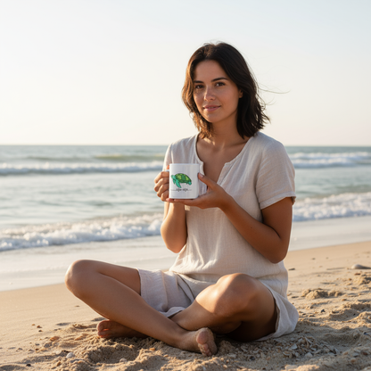 Woman sitting on the beach holding a mug with a green logo