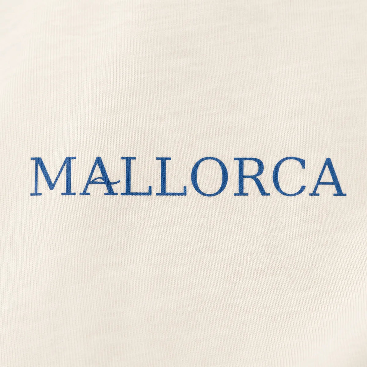 Close-up of a cream-colored fabric surface with the word 'MALLORCA' printed in blue serif letters across the center.