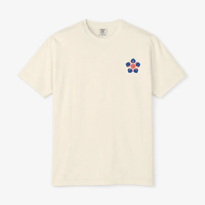 An off-white short-sleeve crewneck t-shirt with a small colorful chest graphic on the left side, displayed against a light gray background.