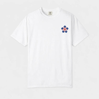 A white short-sleeve crewneck t-shirt featuring a small embroidered flower graphic on the left chest with blue petals, a red center, and yellow accents, displayed against a clean white background.