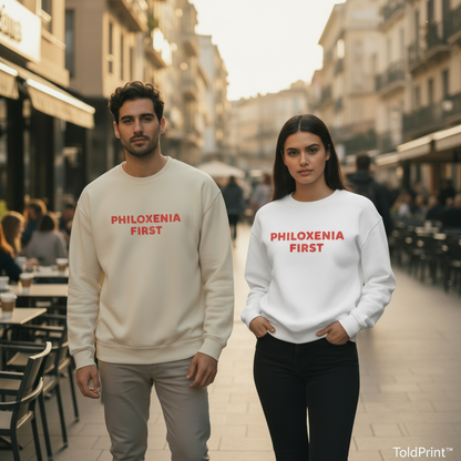Two people wearing sweatshirts with 'PHILOXENIA FIRST' text on a city street.
