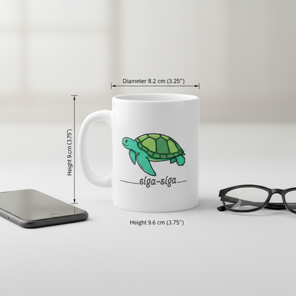 White mug with a green turtle design and 'siga-siga' text, shown with measurements and a phone and glasses for scale.