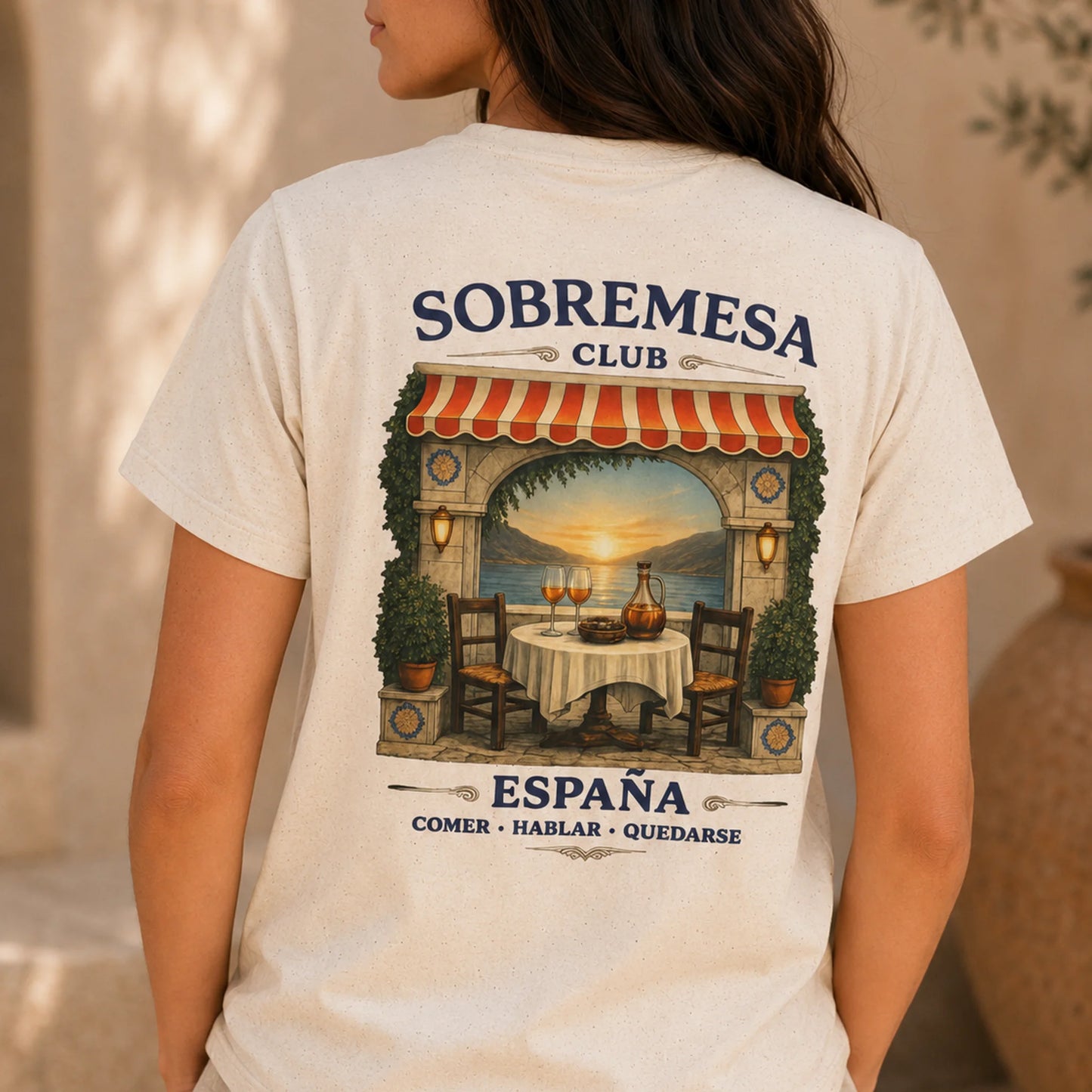 TP HERO: A woman wearing a cream-colored t-shirt, viewed from the back. The shirt features a large graphic print of a Spanish restaurant patio with a sunset view, and the text 'SOBREMESA CLUB' and 'ESPAÑA COMER • HABLAR • QUEDARSE'.