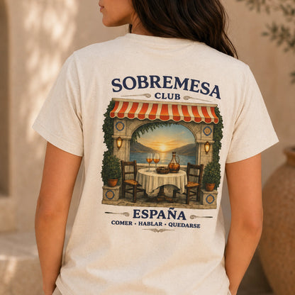 TP HERO: A woman wearing a cream-colored t-shirt, viewed from the back. The shirt features a large graphic print of a Spanish restaurant patio with a sunset view, and the text 'SOBREMESA CLUB' and 'ESPAÑA COMER • HABLAR • QUEDARSE'.