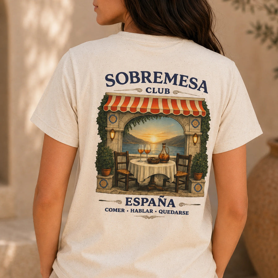 TP HERO: A woman wearing a cream-colored t-shirt, viewed from the back. The shirt features a large graphic print of a Spanish restaurant patio with a sunset view, and the text 'SOBREMESA CLUB' and 'ESPAÑA COMER • HABLAR • QUEDARSE'.