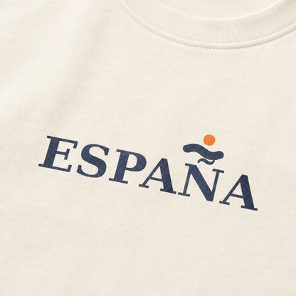 Close-up of a cream-colored t-shirt featuring the word 'ESPAÑA' printed in navy blue across the chest, with a small orange sun and blue wave graphic above the 'A'.