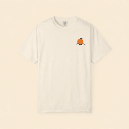 An off-white short-sleeve crewneck t-shirt featuring a small graphic of an orange on a black branch on the left chest, displayed against a solid cream background.