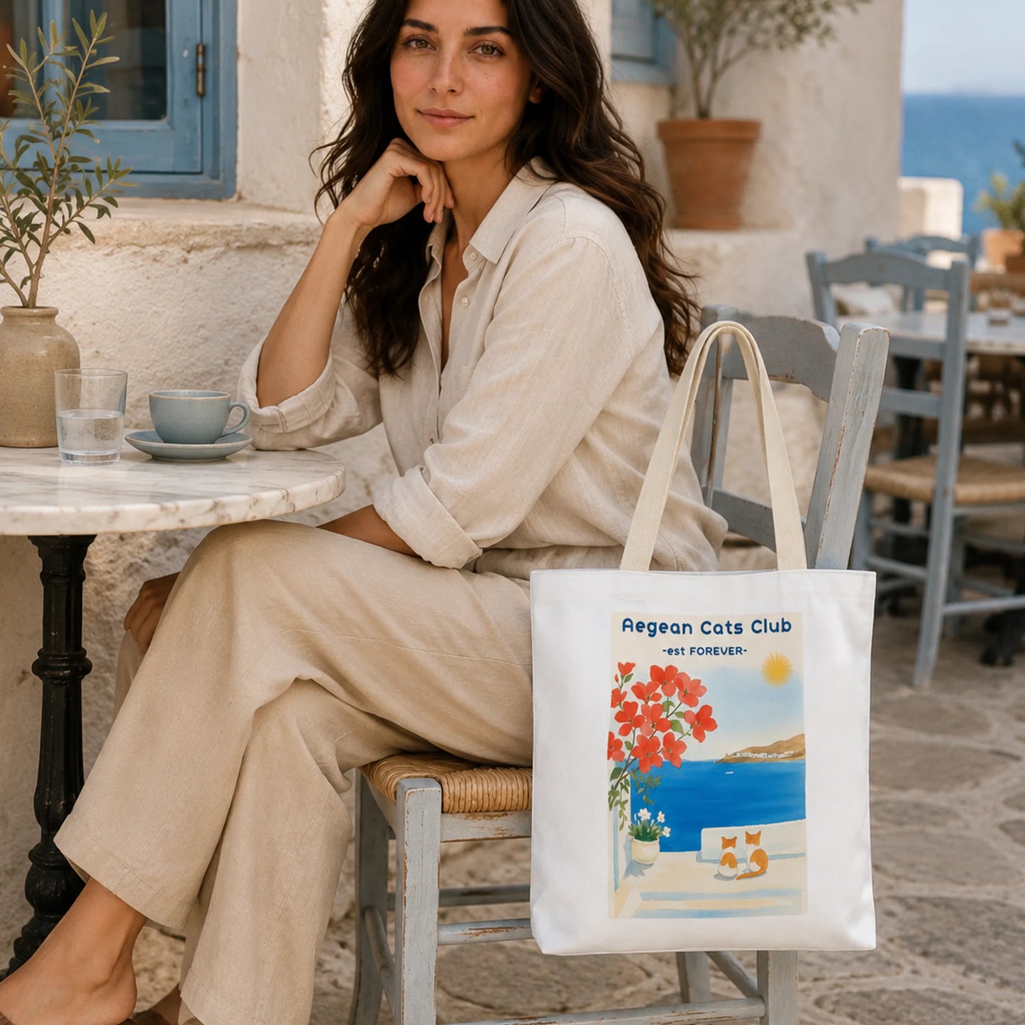 Woman sitting at an outdoor cafe with a tote bag featuring a scenic design.