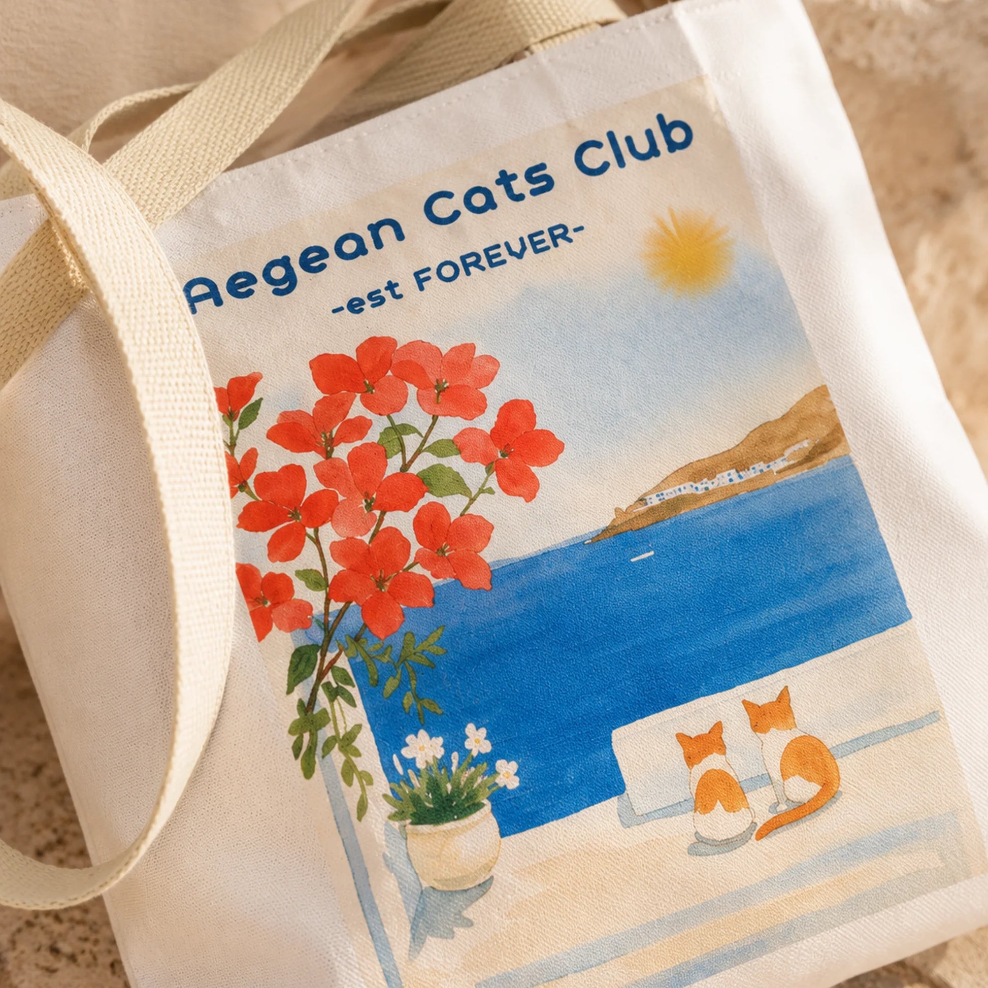 Tote bag with Aegean Cats Club design featuring a cat, flowers, and ocean.