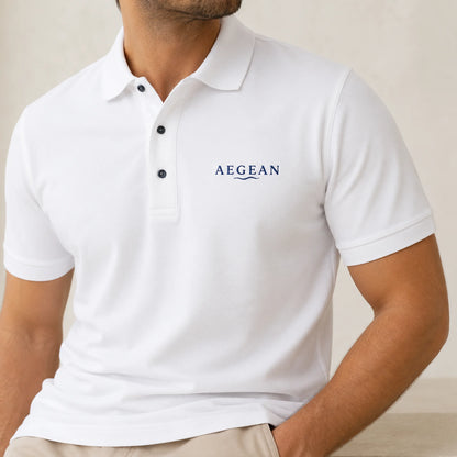 TP HERO: A man wearing a white short-sleeve polo shirt with the brand name 'AEGEAN' printed in navy blue on the left chest, paired with beige trousers against a neutral beige background.