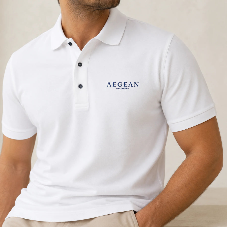 TP HERO: A man wearing a white short-sleeve polo shirt with the brand name 'AEGEAN' printed in navy blue on the left chest, paired with beige trousers against a neutral beige background.