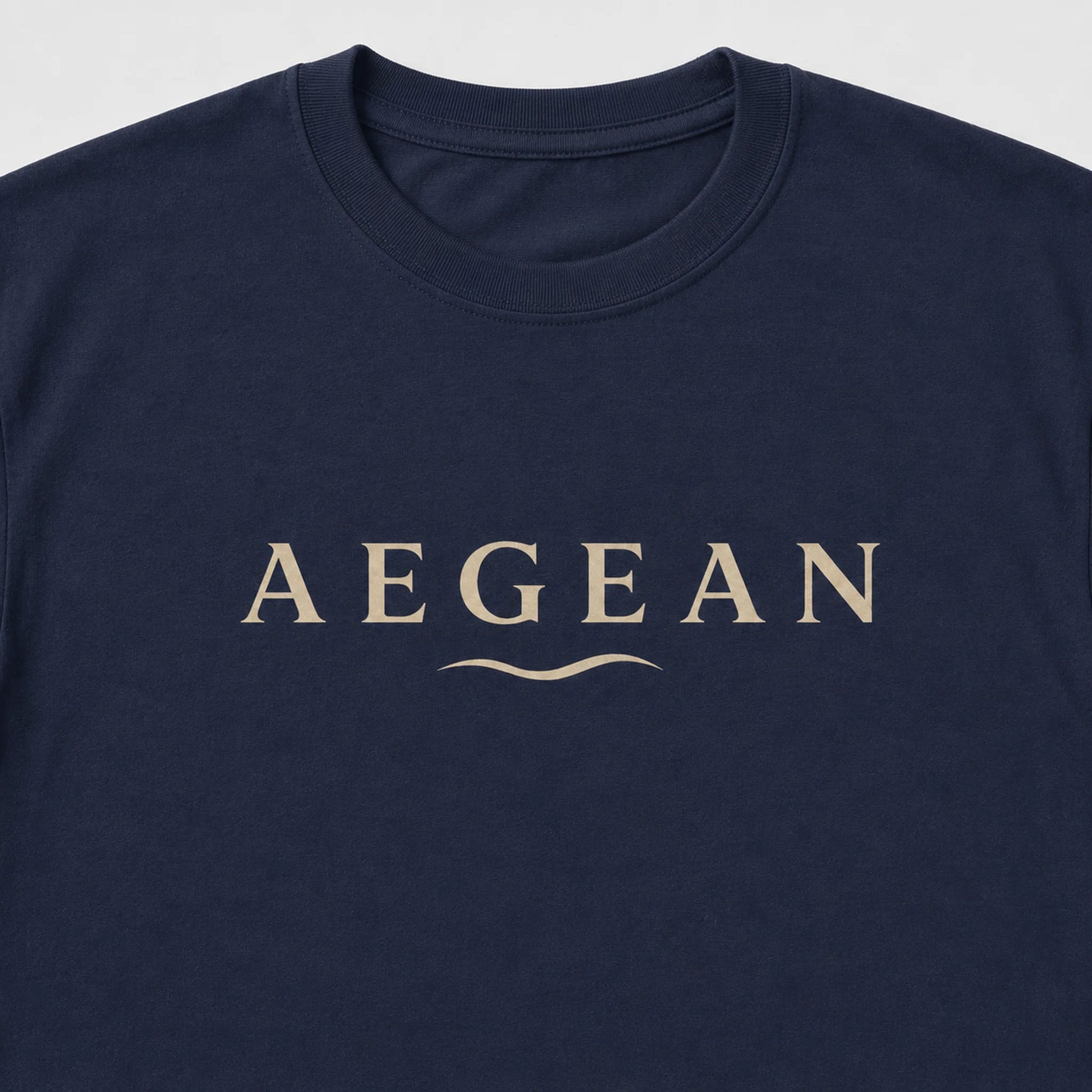 A close-up of a navy blue crewneck t-shirt featuring the word 'AEGEAN' printed in a beige serif font across the chest, with a small wavy line underneath.