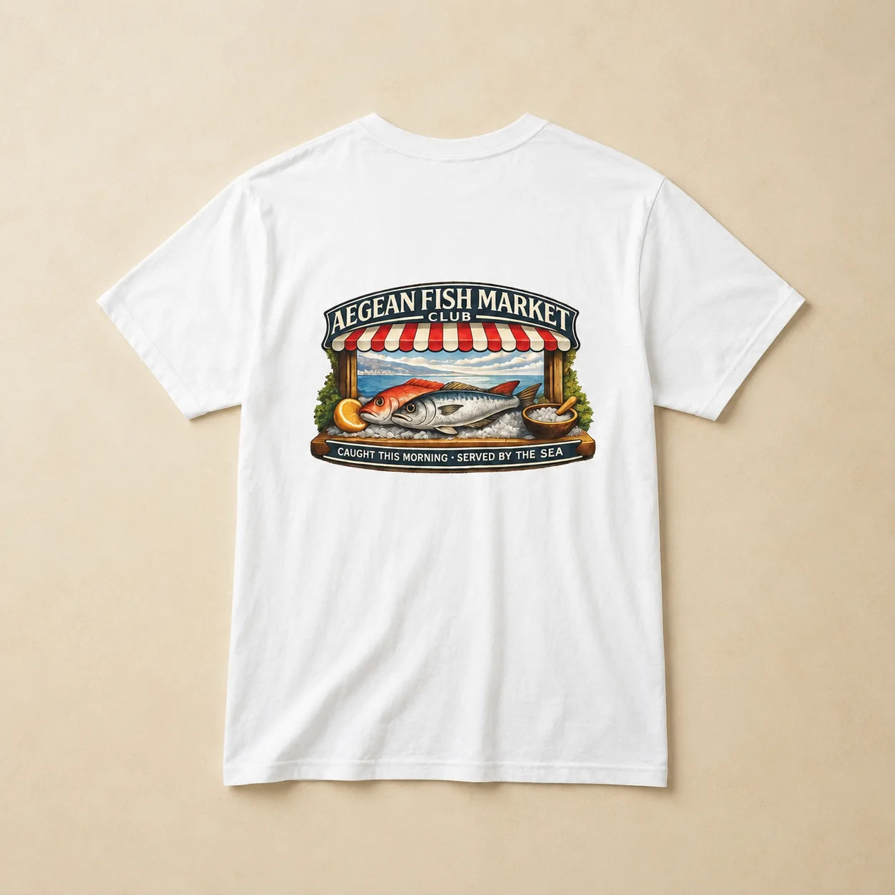 A white short-sleeve crewneck t-shirt laid flat on a light beige background, featuring a colorful graphic print on the front with a fish market scene and the text 'AEGEAN FISH MARKET CLUB'.