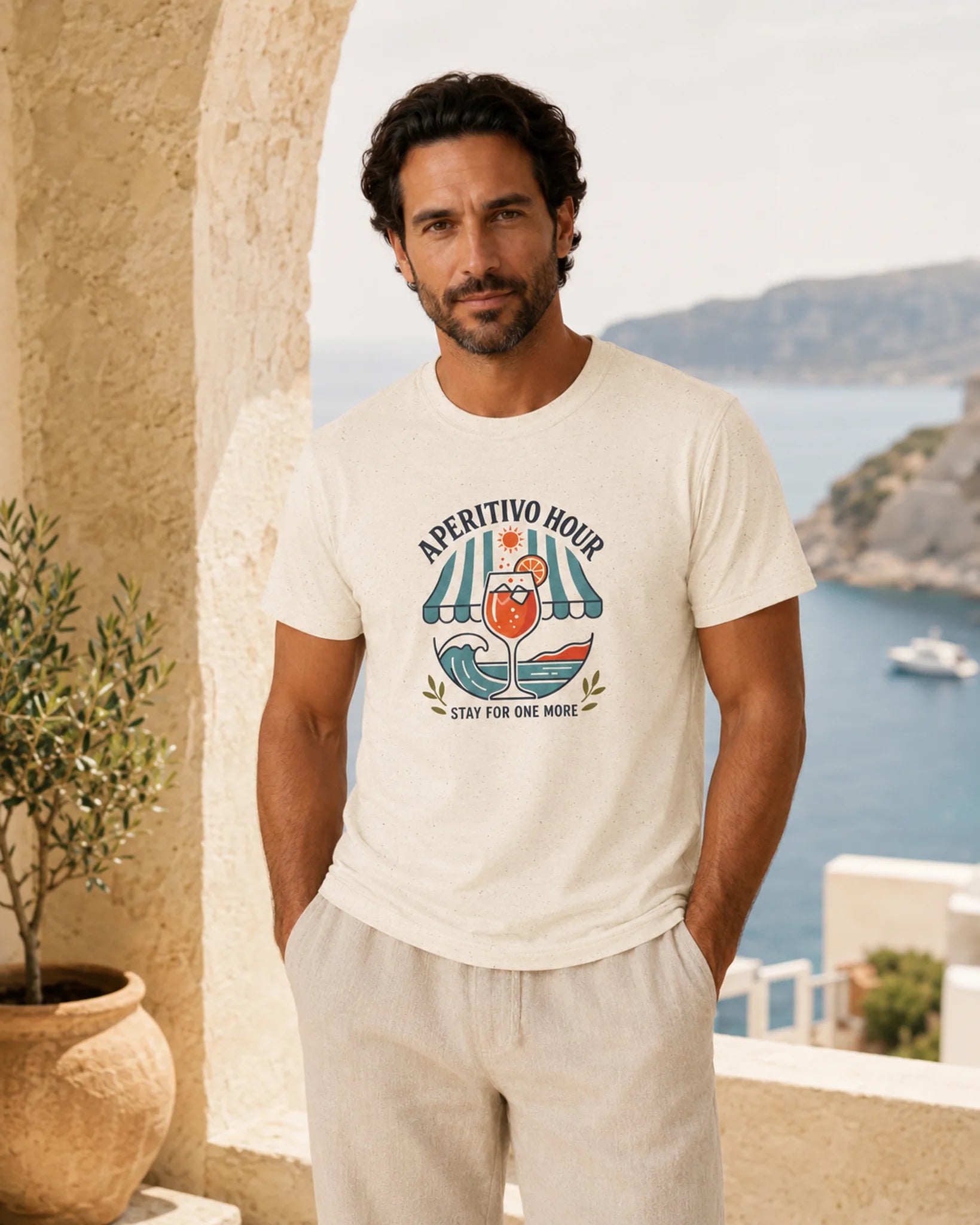 Man wearing a white t-shirt with a graphic design, standing in a scenic location with a view of the sea.