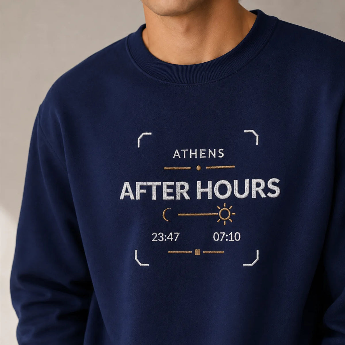 TP HERO: A close-up of a person wearing a navy blue crewneck sweatshirt with a embroidered design on the front that reads 'ATHENS AFTER HOURS' with stylized white and orange text and clock elements.