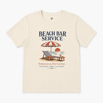 An off-white crewneck t-shirt featuring a retro beach bar graphic with the text 'BEACH BAR SERVICE' and a vintage illustration of a striped umbrella, lounge chair, and sunset.