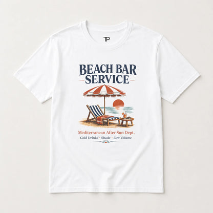 A white short-sleeve crewneck t-shirt featuring a retro-style graphic print of a beach bar scene with the text 'BEACH BAR SERVICE' and a vintage illustration of a striped umbrella, lounge chair, and sunset.