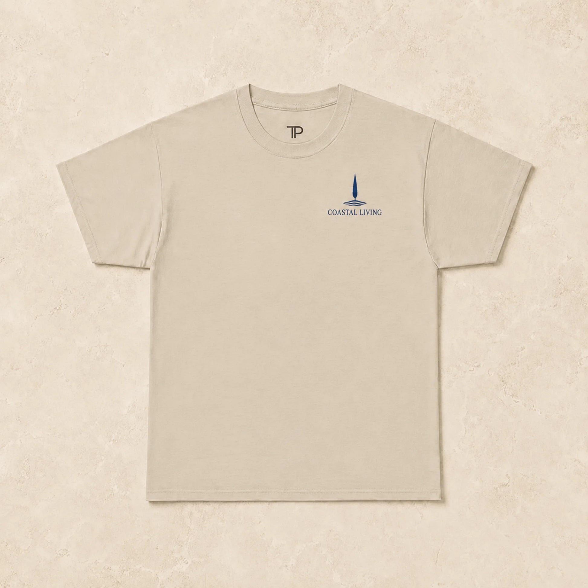 Flat lay of a sand t-shirt with 'Coastal Living' design