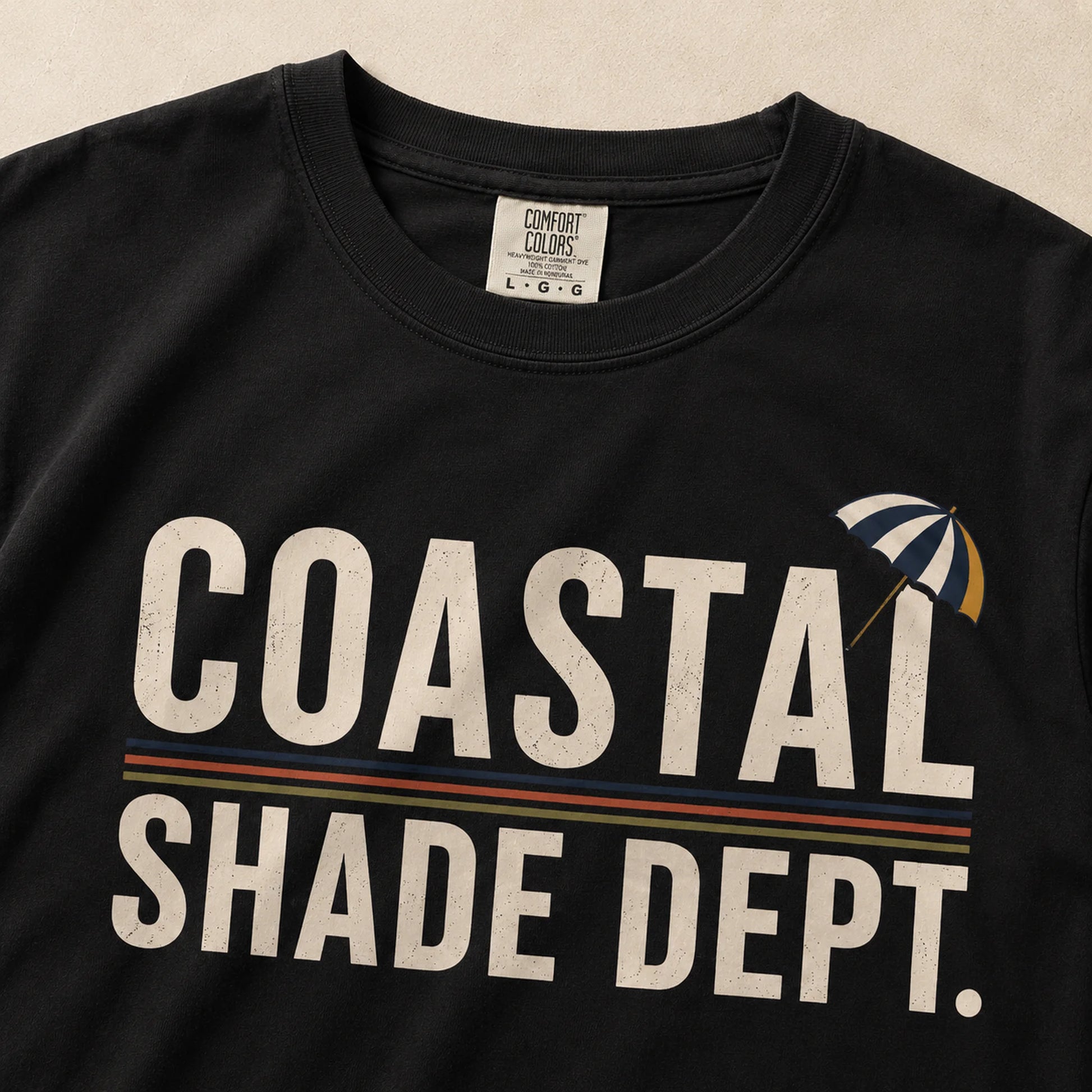 Close-up of Coastal Shade Dept print on black T-shirt showing distressed lettering and umbrella detail