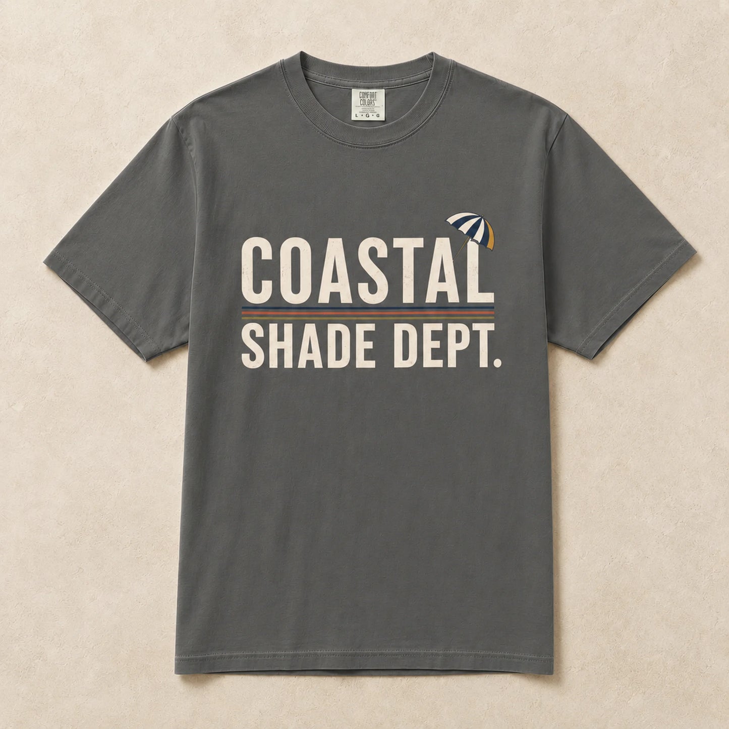 Charcoal Coastal Shade Dept graphic T-shirt laid flat with retro seaside umbrella graphic