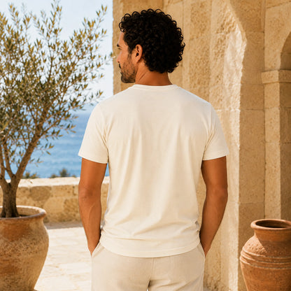 Man in a white t-shirt standing outdoors with a scenic background