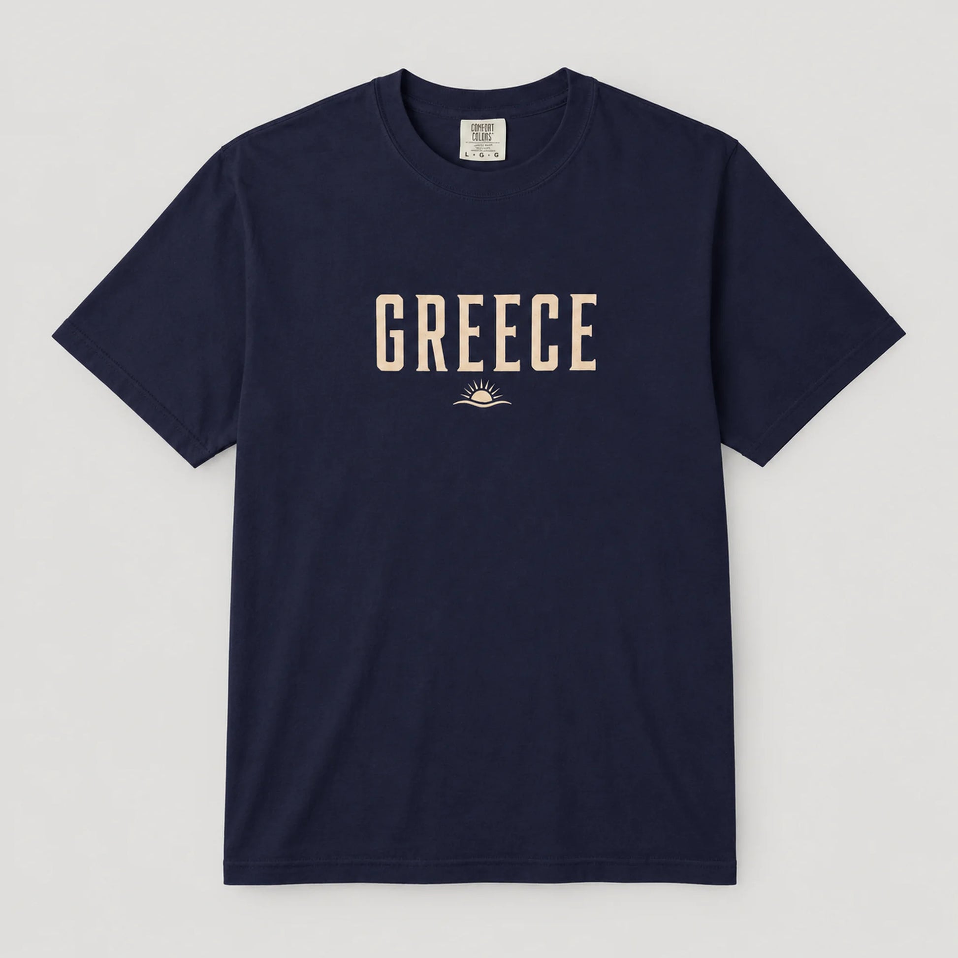 A navy blue short-sleeve crewneck t-shirt with 'GREECE' printed in beige block letters and a small sun graphic on the chest, displayed flat against a light gray background.