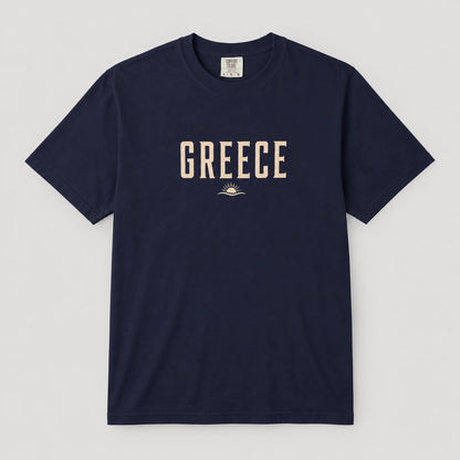 A navy blue short-sleeve crewneck t-shirt with 'GREECE' printed in beige block letters and a small sun graphic on the chest, displayed flat against a light gray background.